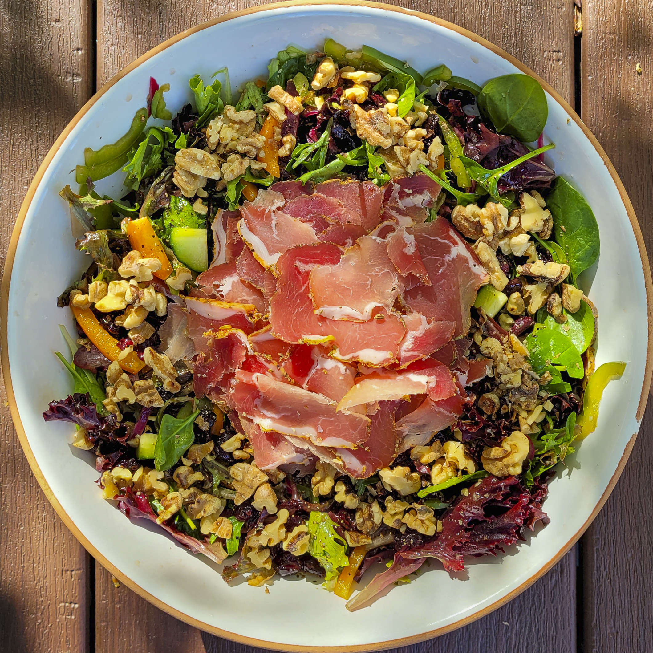 A salad made up of a commercial spring salad mix, cured beef loin, green and orange bell peppers, cucumber, cranberries, and toasted walnuts, with a dressing of red wine vinegar and oliver oil.